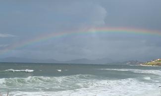 A ranbow above frothy waves.